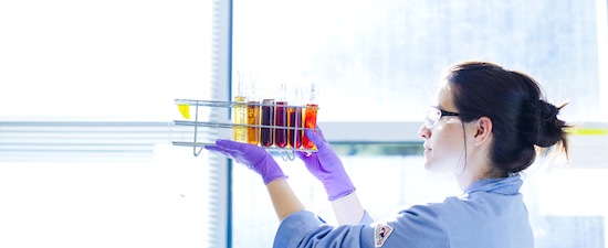 Clinician in a lab coat, holding up testing vials 